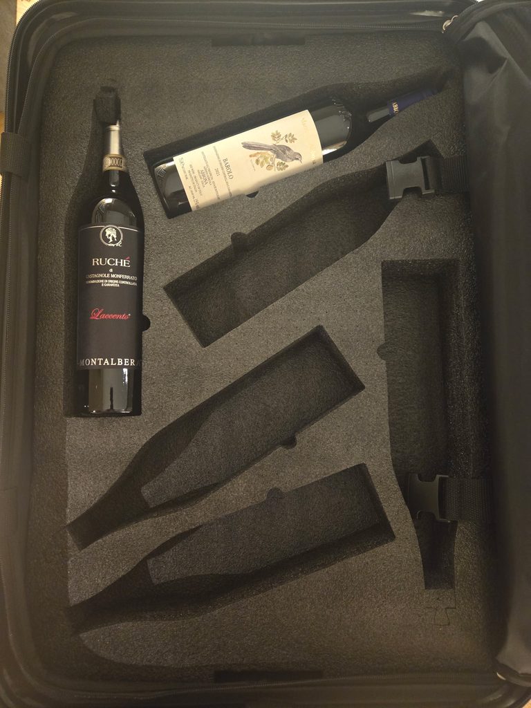 The interior foam insert of the Flies With Wine travel suitcase holding the first two bottles of wine, including a bottle of Ruché and a bottle of Barolo.